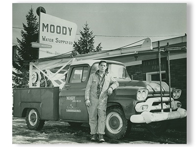 James Moody the founder of Moody and Associates groundwater and environmental professionals since 1891 standing next to old pickup truck outside of water supply company store work for the company now in Houston PA